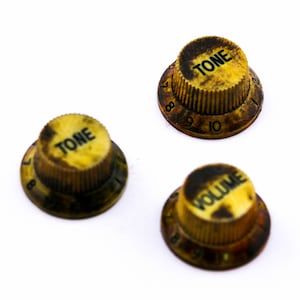 Könnte beinhalten: Drei Vintage-Gitarrenknöpfe mit schwarzem Text auf gelbem Hintergrund. Die Knöpfe sind mit "TONE" und "VOLUME" beschriftet und haben die Zahlen 8, 9 und 10 um die Ränder gedruckt.