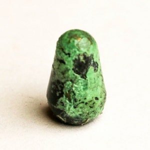 May include: A small, green and black, irregularly shaped, ceramic, bottle stopper.