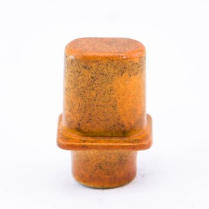 May include: A small, ceramic, orange-brown bottle stopper with a square base.