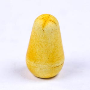 May include: A pear-shaped, yellow-toned object with a cross-shaped marking at the top. The surface has a speckled texture, and the bottom has a subtle horizontal line. The object is set against a plain white background.