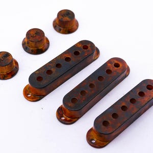 Könnte beinhalten: Vier Gitarren-Tonabnehmer aus Schildpatt und drei Knöpfe mit den Aufschriften "Volume", "Tone" und "Tone".
