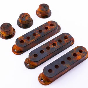Può includere: Quattro coperture per pickup di chitarra con un motivo a tartaruga e tre manopole etichettate "Volume", "Tone" e "Tone".