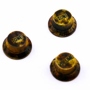 May include: Three vintage guitar knobs with black text on a yellow background. The knobs are labeled "TONE" and "VOLUME".