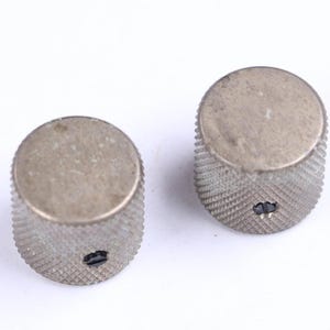 May include: Two vintage silver-toned guitar knobs. The knobs have a textured, diamond-patterned grip around the sides and a flat top. Each knob has a small, dark-colored set screw hole.