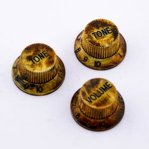 Könnte beinhalten: Drei vintage goldfarbene Gitarrenknöpfe mit schwarzer Beschriftung. Die Knöpfe sind mit "TONE" und "VOLUME" beschriftet und haben die Zahlen 8, 9 und 10 am Rand.