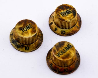 May include: Three vintage gold-colored guitar knobs with black lettering. The knobs are labeled "TONE" and "VOLUME" with numbers 8, 9, and 10 around the edges.