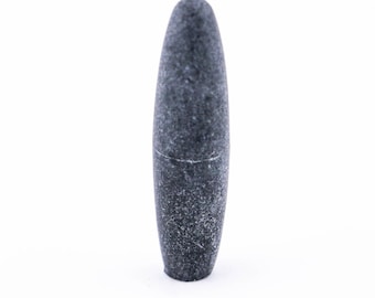 Puede incluir: Una piedra lisa de color gris oscuro con forma de óvalo redondeado. La piedra es natural, sin pulir y tiene una textura rugosa.