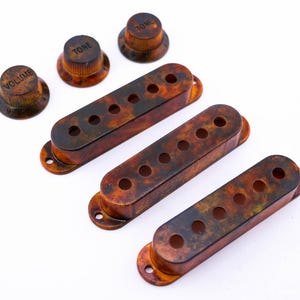 Könnte beinhalten: Drei Gitarren-Tonabnehmerabdeckungen aus Schildpatt und drei Knöpfe mit der Aufschrift "Volume" und "Tone".