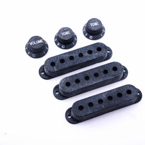 Könnte beinhalten: Drei schwarze Gitarren-Tonabnehmerabdeckungen und drei schwarze Knöpfe mit weißer Beschriftung. Die Knöpfe sind mit "Volume" und "Tone" beschriftet.