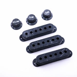 May include: Three black guitar pickup covers with six holes each and three black knobs labeled "Volume", "Tone", and "Tone".