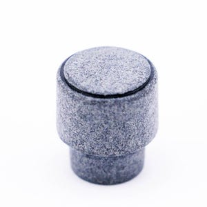 May include: A gray and black round bottle stopper with a textured surface.