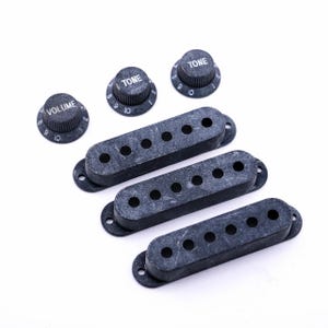May include: Three black guitar pickup covers and three black knobs with white lettering. The knobs are labeled "Volume" and "Tone".