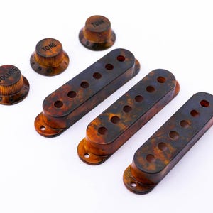 Könnte beinhalten: Satz mit drei Gitarren-Tonabnehmerabdeckungen aus Schildpatt und drei Knöpfen mit den Beschriftungen "Volume", "Tone" und "Tone".
