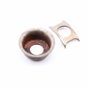 May include: Two metal parts for a guitar, one is a round cup with a hole in the center, the other is a flat, curved piece with a hole in the center.