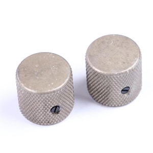 May include: Two silver-colored, cylindrical knobs with a textured, knurled surface. Each knob has a flat top and a small, black screw. The knobs are likely for use on an electronic device or musical instrument.
