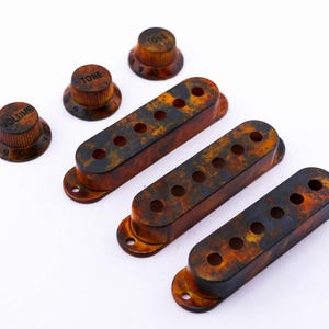 Könnte beinhalten: Drei Gitarren-Tonabnehmerabdeckungen aus Schildpatt und drei Knöpfe für eine Gitarre. Die Knöpfe sind mit "Volume" und "Tone" beschriftet.