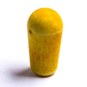 May include: A yellow, cylindrical object with a rounded top. The object has a textured surface and appears to be made of a solid material. The color is a warm, golden yellow with some darker spots.