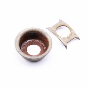 May include: Two metal parts, one a cup-shaped washer with a rusty interior and the other a flat, rectangular piece with a hole in the center.
