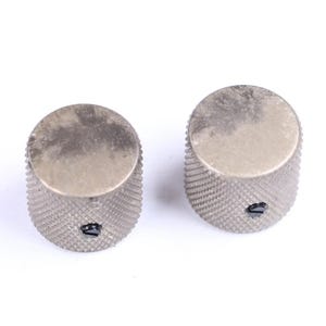 May include: Two silver-colored control knobs with a textured, ridged body and a flat top. The knobs have a small black indicator arrow. The knobs are likely for an electronic device, such as a guitar or amplifier.