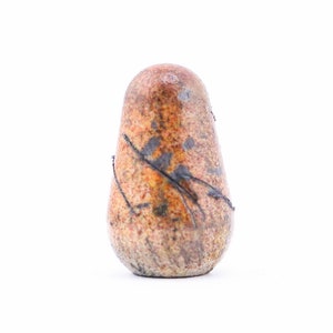 May include: A small, brown, ceramic vase with a textured surface and black lines. The vase is shaped like a rounded egg.