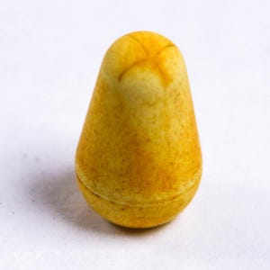 May include: A yellow pear-shaped object with a textured surface and a cross-shaped marking on top. The object appears to be a decorative item or a small container, possibly a trinket box or a decorative piece.