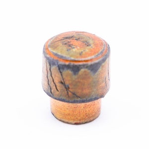 May include: A ceramic bottle stopper with a brown, orange, and black glaze. The top of the stopper is round and has a slightly raised edge. The bottom of the stopper is flat.