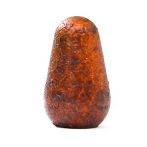 May include: A close-up of a wooden, teardrop-shaped object with a textured surface. The object is primarily brown with darker, almost black, markings. The shape is smooth and rounded at the top, tapering to a slightly wider base.