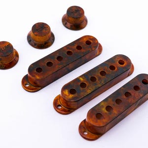 Könnte beinhalten: Drei Gitarren-Tonabnehmerabdeckungen aus Schildpatt und drei Knöpfe für eine Gitarre. Die Knöpfe sind mit "Volume" und "Tone" beschriftet.