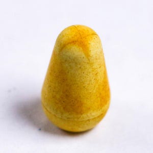 May include: A close-up of a yellow, pear-shaped object with a rounded top. The object has a textured surface with darker yellow and brown spots. The background is plain white.