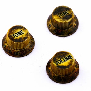 Könnte beinhalten: Drei goldfarbene Vintage-Gitarrenknöpfe mit schwarzer Beschriftung. Die Knöpfe sind mit "TONE" und "VOLUME" beschriftet und haben die Zahlen 8, 9 und 10 am Rand.