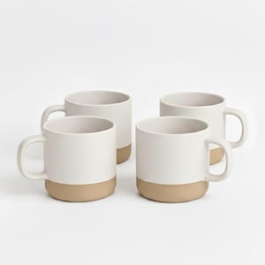 May include: Four white ceramic mugs with a beige base and a curved handle. The mugs are evenly spaced against a white background. The mugs are designed for hot beverages.