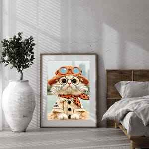 May include: A framed wall art print featuring a fluffy cat wearing a tan button-down shirt, an orange polka-dot neckerchief, and a matching orange hat with blue-rimmed goggles. The cat has large round glasses and a light-colored coat.