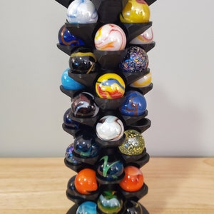 May include: A black marble display stand with multiple tiers, holding a variety of colorful marbles. The stand is made of plastic and has a circular base. The marbles are arranged in a spiral pattern, with each tier holding a different color.