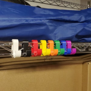 May include: A set of ten colorful plastic hooks, in a rainbow pattern, hanging on a metal shelf. The hooks are designed to hang items on a wire shelf.