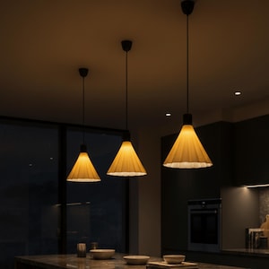 May include: Three pendant lights with pleated, cone-shaped shades in a warm yellow hue hang from black cords. The lights are suspended over a dark countertop, creating a modern and inviting ambiance. The shades have a textured appearance.