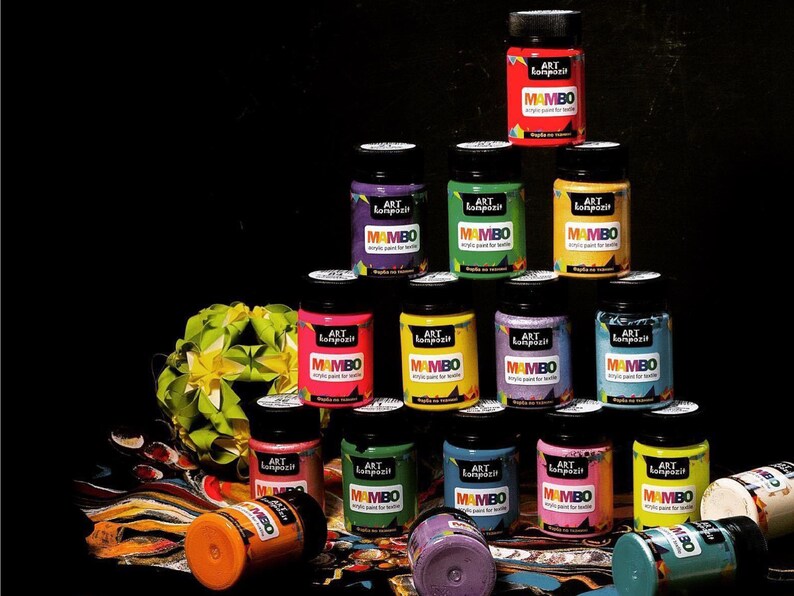 May include: A collection of 14 small paint bottles with colourful lids. The bottles are labelled "Art Lonpozit Mambo Acrylic Paint for Textile".