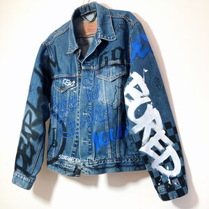 May include: A blue denim jacket with black and white graffiti and blue and white lettering. The lettering includes the words "SOUNDGARDEN", "HOME", "FOR", "ALWAYS", "NOW", and "WORKED".