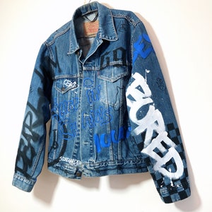 May include: A blue denim jacket with black and white graffiti and blue and white lettering. The lettering includes the words "SOUNDGARDEN", "HOME", "FOR", "ALWAYS", "NOW", and "WORKED".