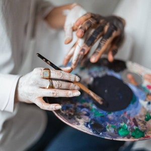 May include: A person's hands holding a paint palette with a variety of colors, including blue, green, and yellow. A paintbrush is resting on the palette.
