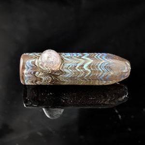 Pode incluir: Um cachimbo de vidro soprado à mão com um padrão de redemoinho de marrom, azul e branco. O cachimbo tem uma ponta arredondada e transparente e um detalhe esférico prateado. O design apresenta um padrão de ondas, em fundo preto.