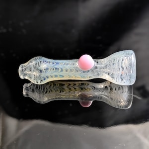 May include: A clear glass pipe with a white and blue swirl design. The pipe has a pink glass ball on the end.