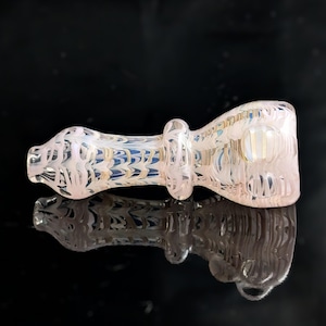 Pode incluir: Um cachimbo de vidro transparente com um design em espiral rosa e branco. O cachimbo tem uma tigela arredondada e um longo caule cilíndrico. O design inclui detalhes em azul e dourado. O cachimbo é refletido em uma superfície preta.