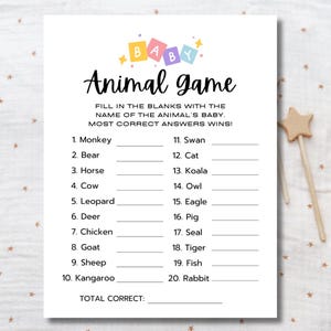 May include: A white baby shower game card with the title "Animal Game" in black script. The card features fill-in-the-blank questions about animal babies. Colorful block letters spell "BABY" at the top. A wooden star wand is in the background.