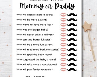 Puede incluir: Una tarjeta blanca con el texto "GUESS WHO Mommy or Daddy" y preguntas sobre los padres del bebé. Las preguntas van acompañadas de imágenes de labios y bigotes. Una varita de estrella de madera está en el fondo.
