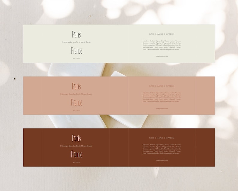 May include: Three rectangular labels with a brown, beige, and white background. The labels feature the text "Paris, France" and "Drinking a glass of red in Le Marais district". The labels also include the text "Rose | Smoke | Espresso" and a list of ingredients.
