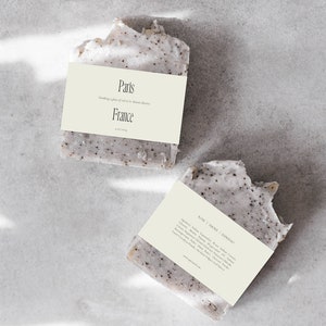 May include: Two bars of handmade soap with a light brown label. The top label reads "Paris" and "Dreaming of a place of old in the Marais district" and "France". The bottom label reads "Rose | Ambre | Figuier" and lists ingredients including shea butter, coconut oil, and olive oil.