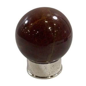 Puede incluir: Un tapón de botella decorativo y esférico. La parte superior es de un material pulido de color marrón oscuro, similar al mármol. La base es de metal brillante de color plateado. El tapón está diseñado para encajar en una botella.