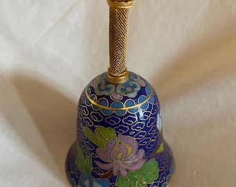 Può includere: Una piccola campana blu e dorata con un motivo floreale. La campana ha una parte superiore decorativa con un design a forma di gabbia.