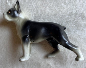 Può includere: Una statuetta in ceramica di un cane Boston Terrier vista di profilo. Il cane presenta un manto bianco e nero con una finitura liscia e lucida, orecchie a punta e occhi dai toni aranciati, in una classica posa vigile con coda corta.