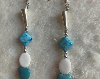 Può includere: Un paio di orecchini pendenti con ganci color argento e perline coniche, seguiti da una perlina blu a forma di diamante, una perlina ovale bianca liscia e una perlina turchese a forma di cuore, con piccole perline distanziatrici color argento.